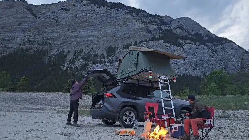 Campfire burning at dusk beside a RAV4 with rooftop tent, mountains in the background